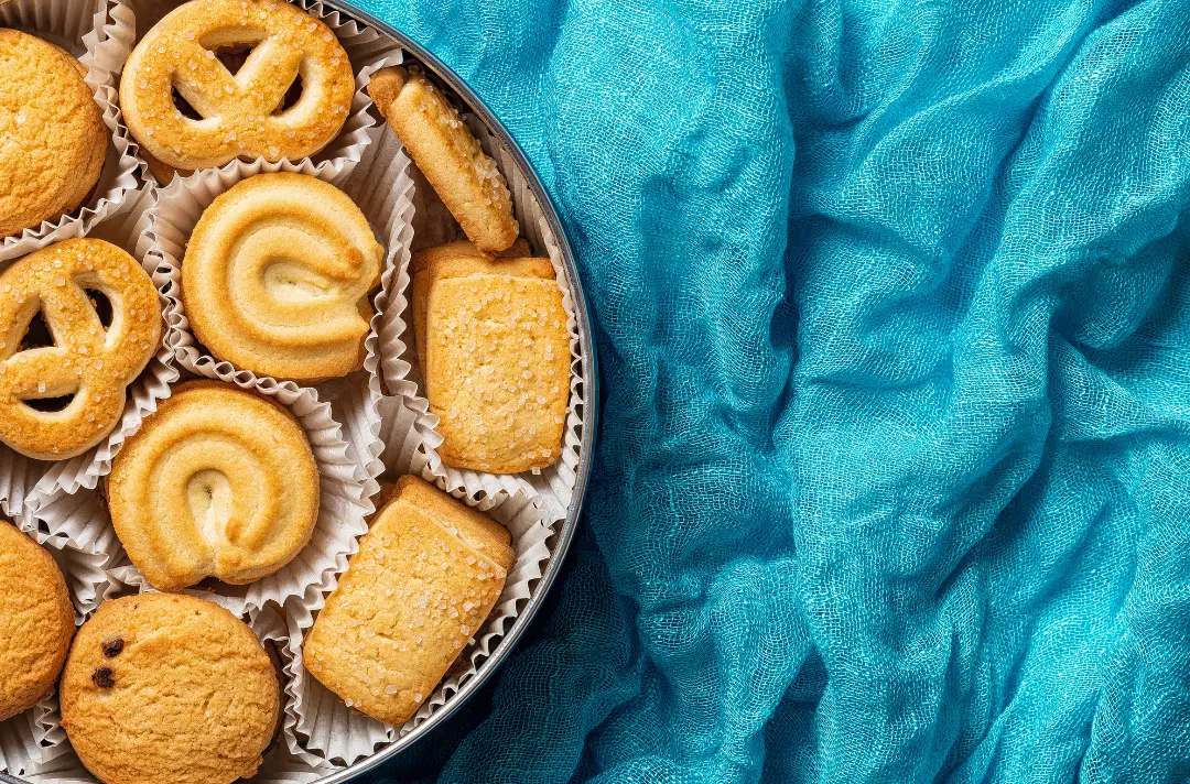 A photo shows a filled biscuit tin atop a vibrant blue fabric.