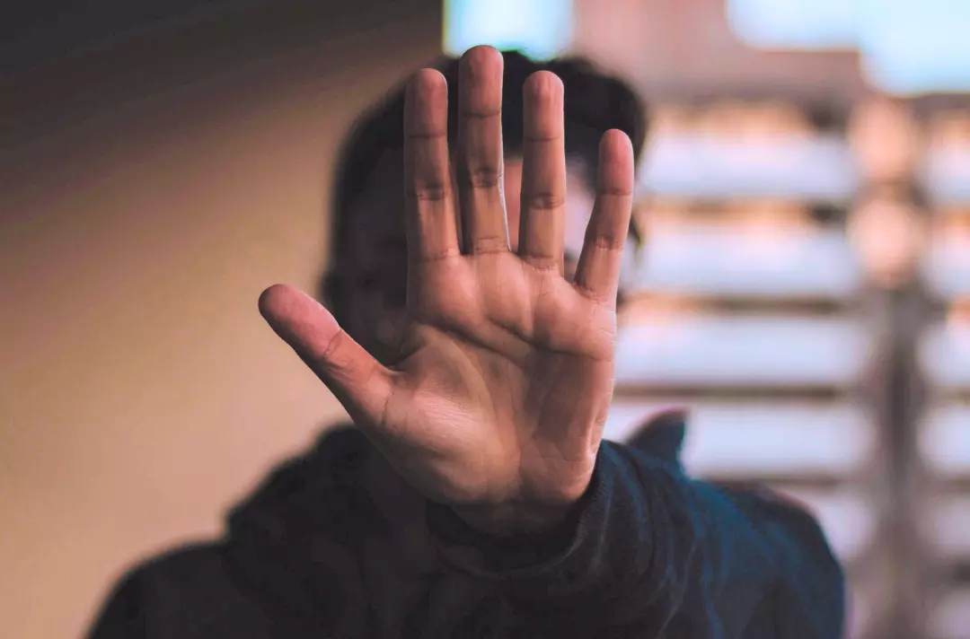 A photo shows someone holding their open hand up in front of their face. 