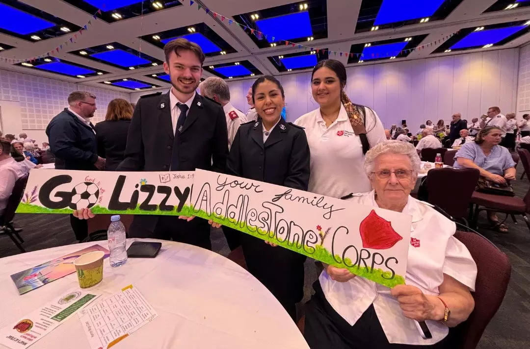 A photo of four people of all ages from Addlestone Corps holding signs to cheer on Lizzy Kitchenside. The signs read: 'Go Lizzy' and 'Your family, Addlestone Corps'