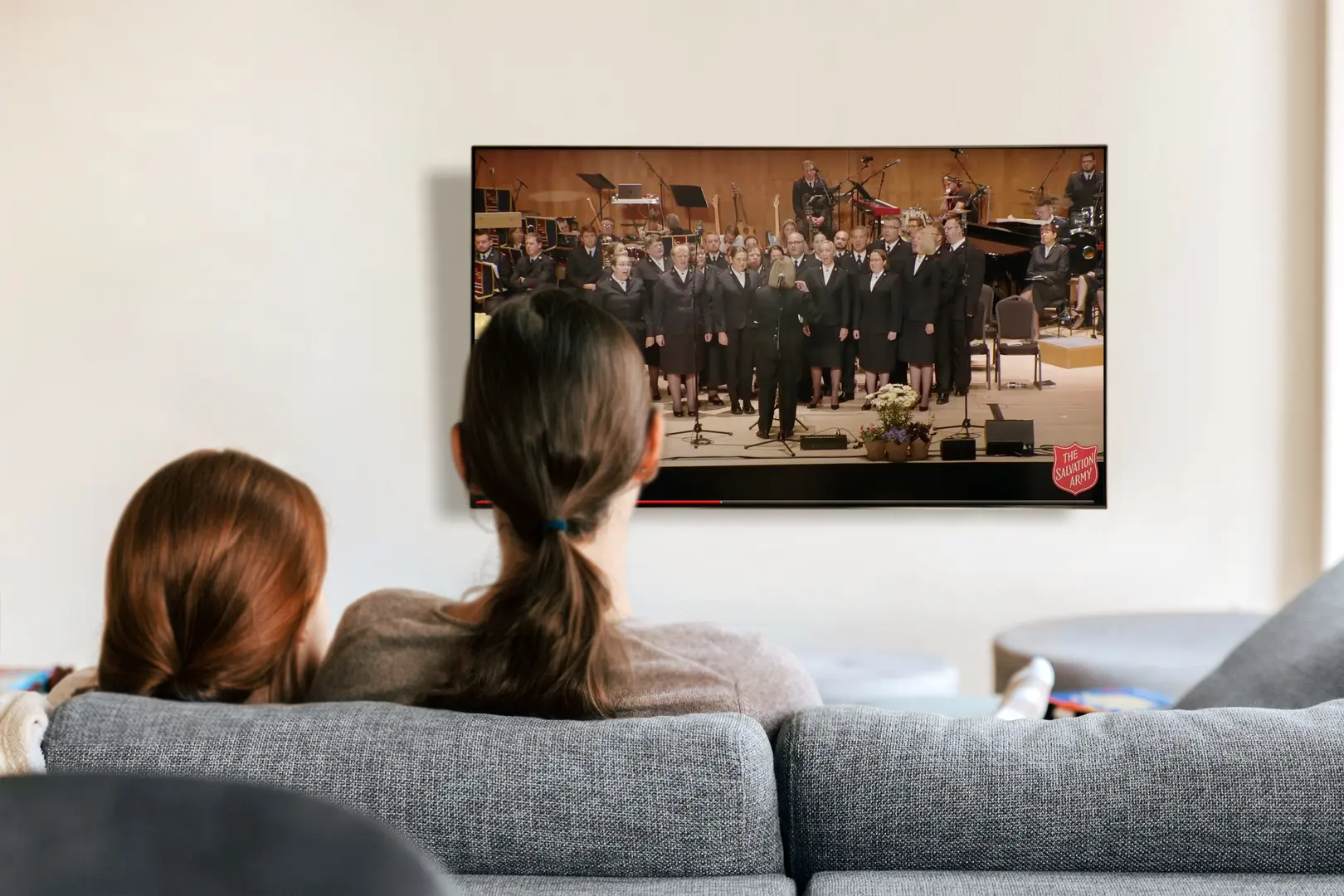 A photo of a mother and daughter sitting on the sofa watching the commissioning livestream