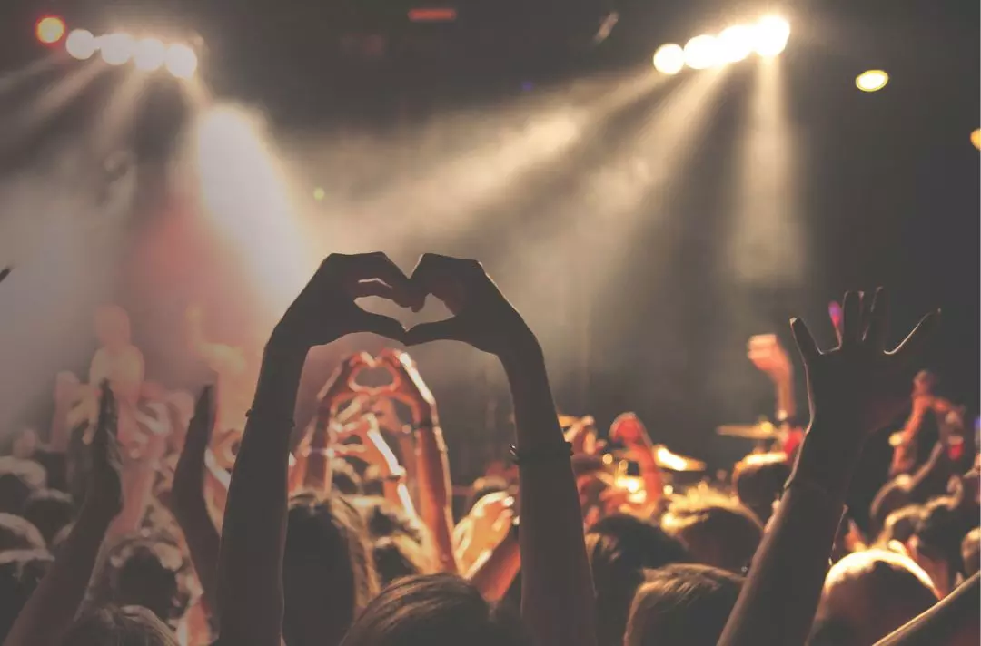 A partygoer makes a heart sign with their hands at a music concert