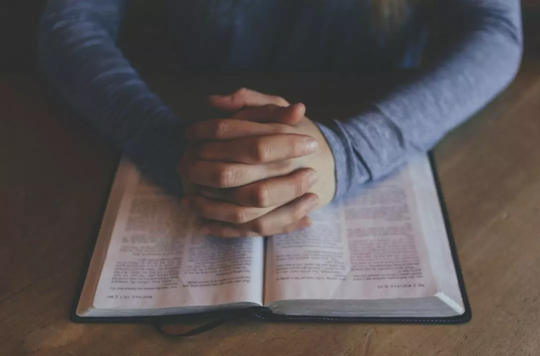 Person praying over Bible with clasped hands