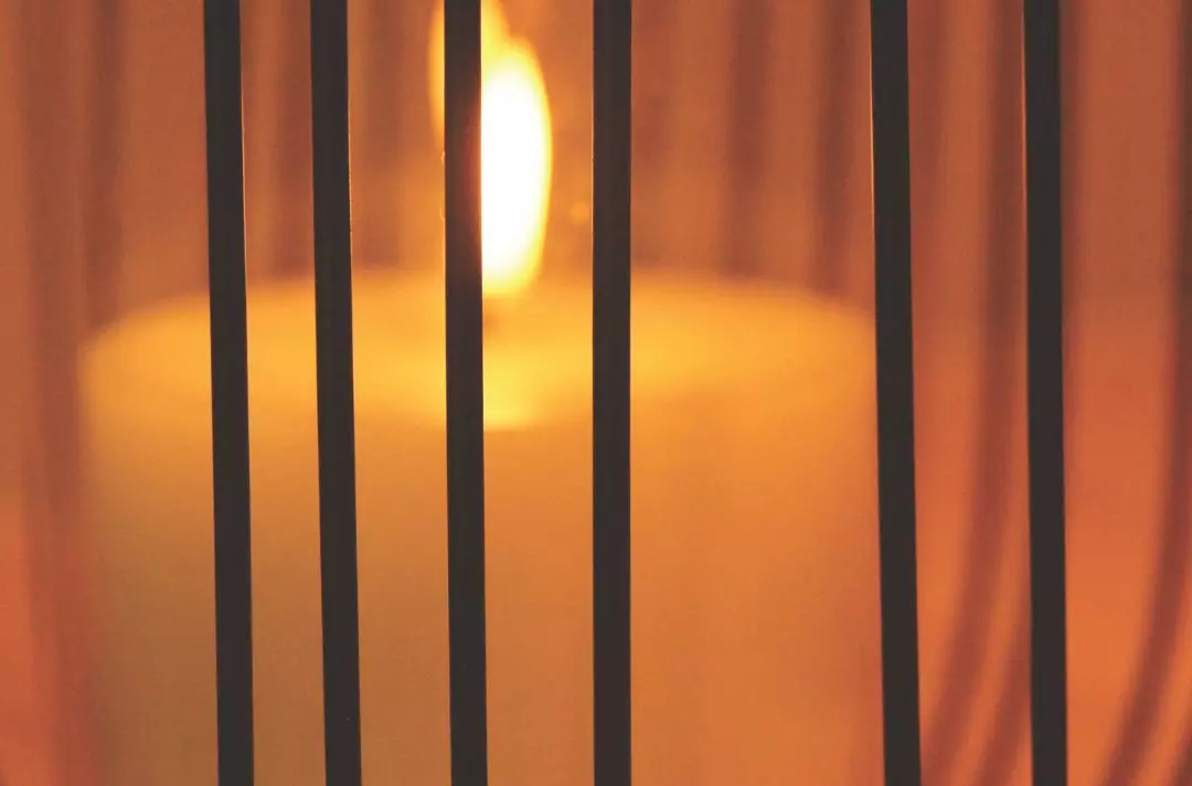 A photo of a candle burning behind bars