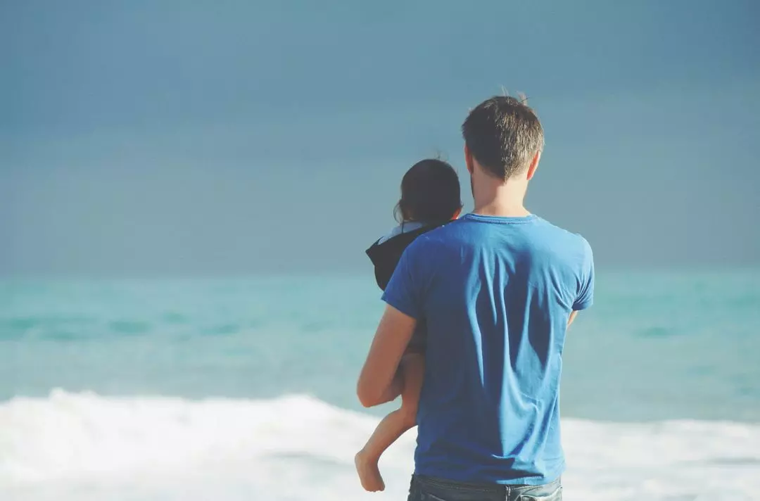 A father holds his child while looking out to sea