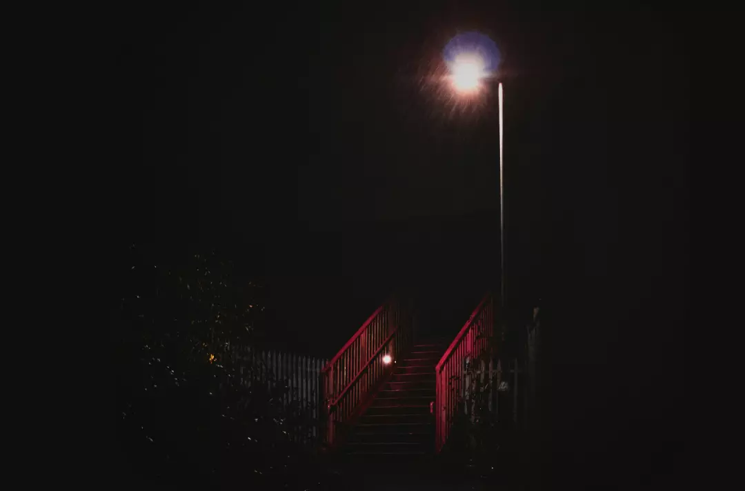 A photo shows a bridge on a dark street. Overhead, a single street light pierces the blackness.