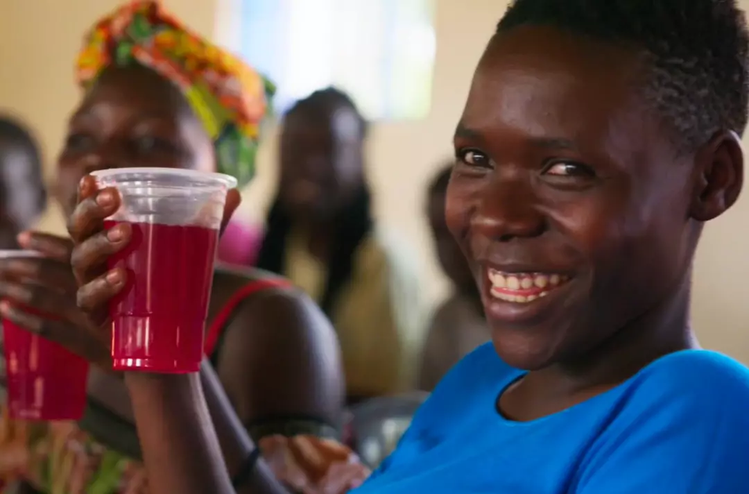 A photo shows someone holding up a clear cup filled with juice and smiling.