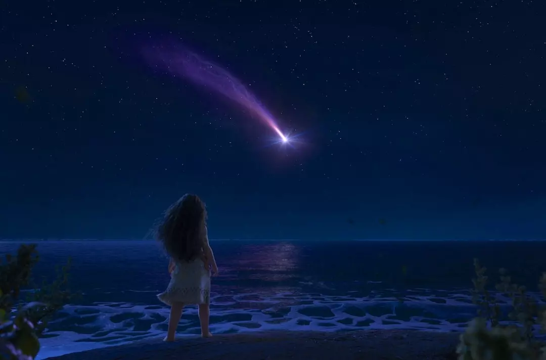 A photo shows a scene from Moana 2. Moana stands at the edge of an island and looks at a shooting star streaking across a starry sky.