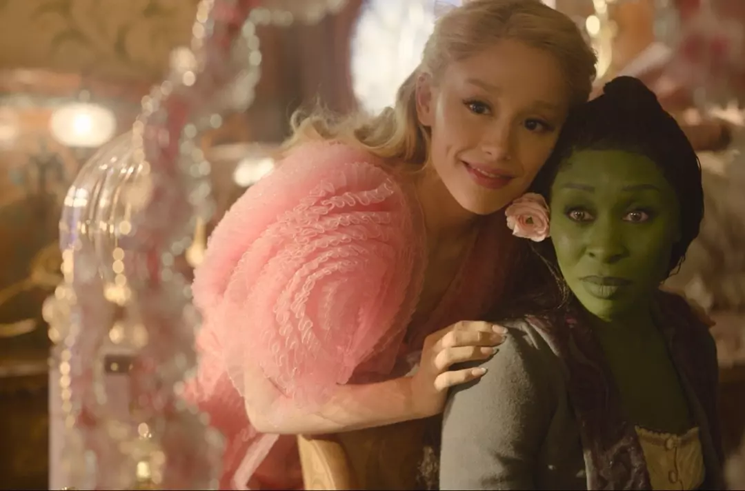 A scene from the movie Wicked shows Glinda and Elphaba looking together in a mirror.