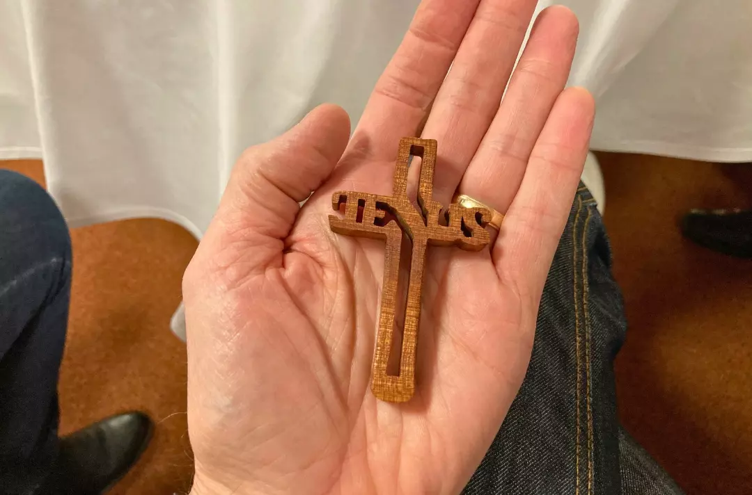 A photo shows an open palm holding a small ornate wooden croos.