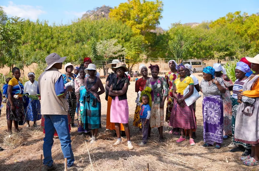 A photo shows a group of people gathered round listening to someone.