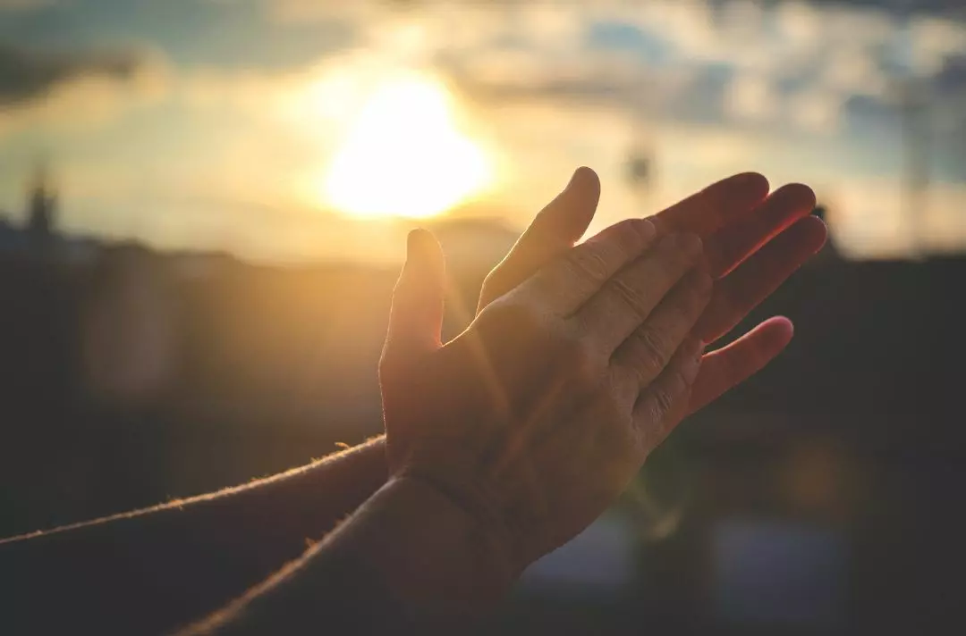 Hands held in prayer in front of sunset
