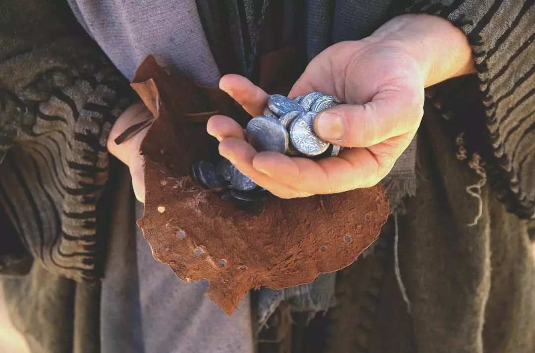 Judas's hands holding silver coins from a leather purse.