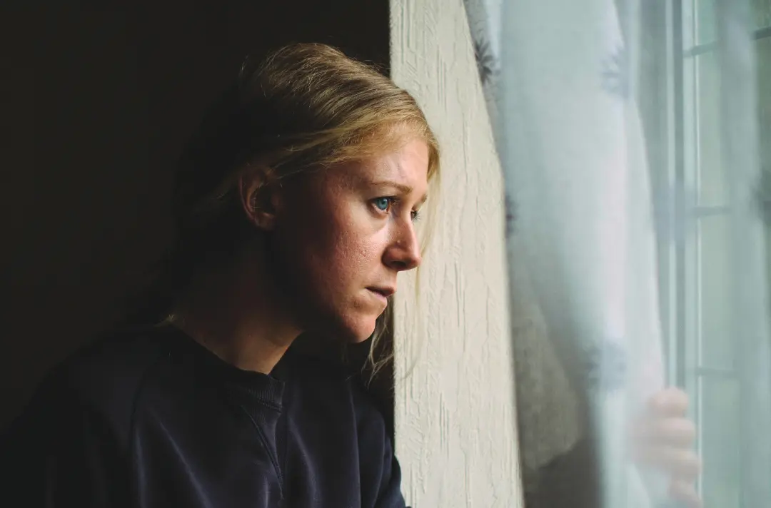 A photo shows someone looking mournfully out of a window.