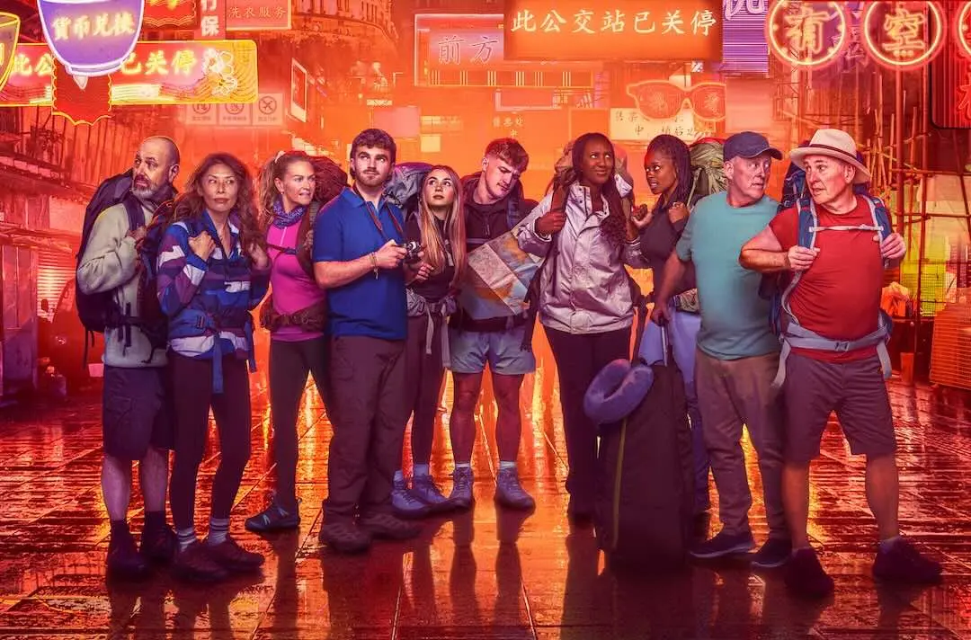 A group of contestants carrying backpacks stand in a neon-lit street looking for directions
