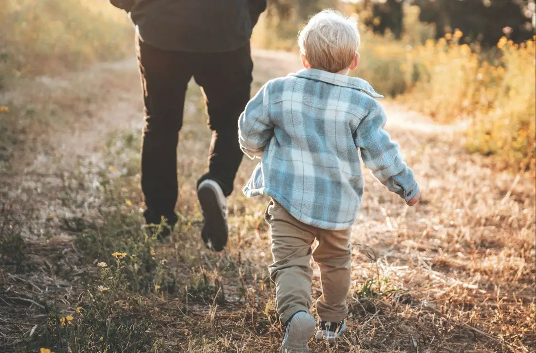 A child follows his father through a field.