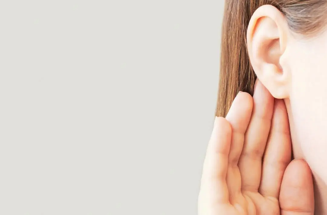 A woman holding her hand to her ear.
