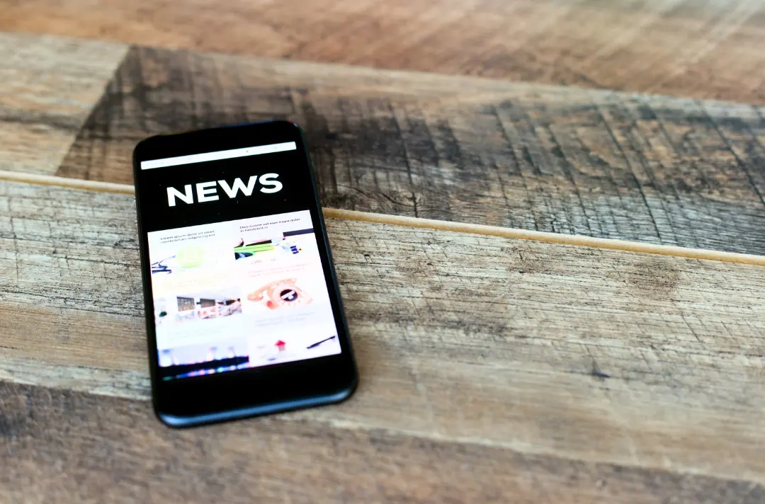 A photo shows a mobile phone lying on a table displaying news.