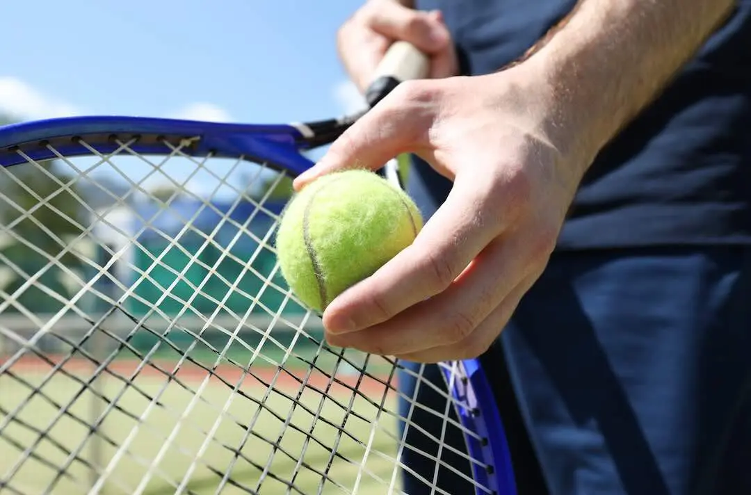 A man holds a tennis ball and racket preparing to serve on a grass court