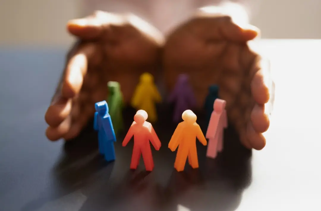 A photo shows a pair of hands wrapping around a diverse collection of small human figures.