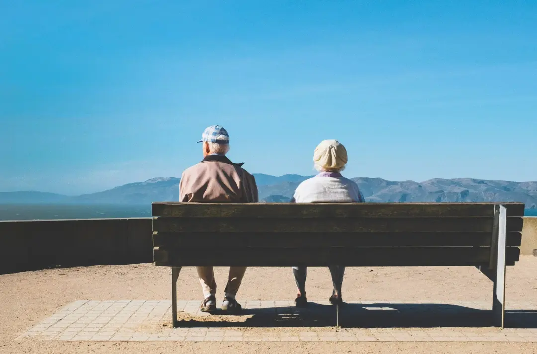 A photo shows two people sat on a bench in front of a brilliant blue sky.