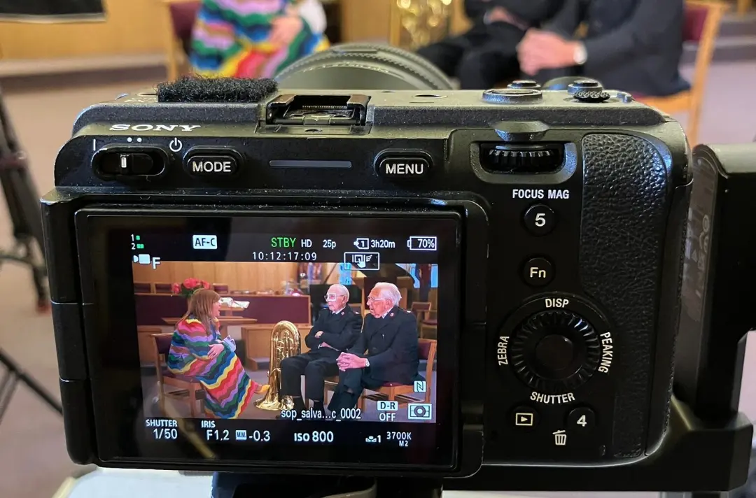 A photo shows a camera with a screen displaying a scene of two Salvationists talking to the host of Songs of Praise.