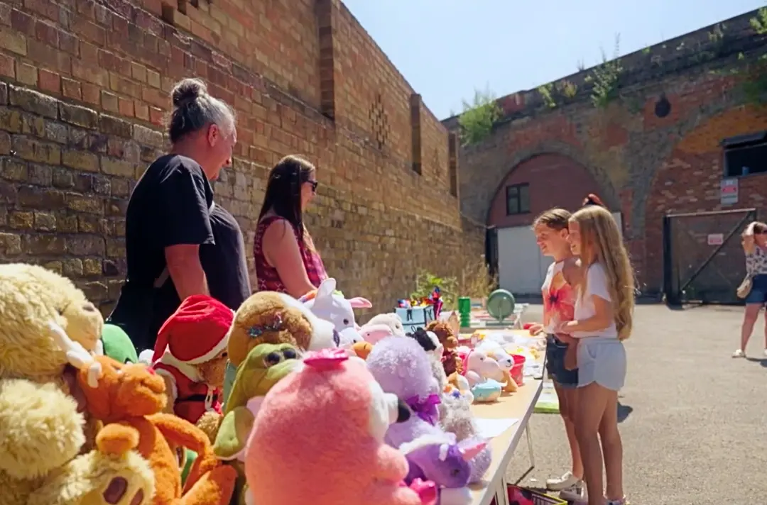 A photo shows two people looking after a stall filled with cuddly toys.