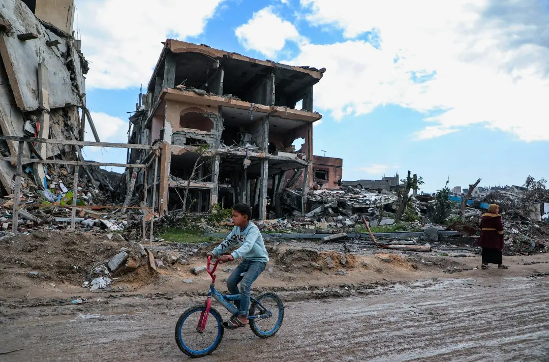 A photo shows a young person cycling through a war-torn street.