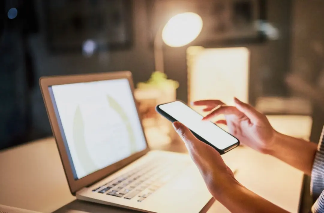 A photo of someone using their phone and laptop