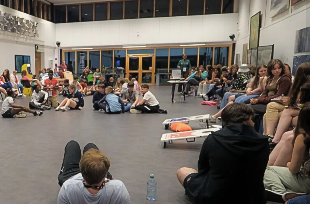 A photo shows a large room with summer school students hanging out together.