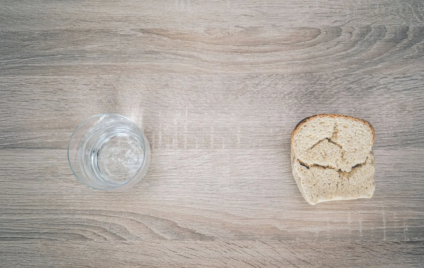 A glass of water and plain bread on a table.