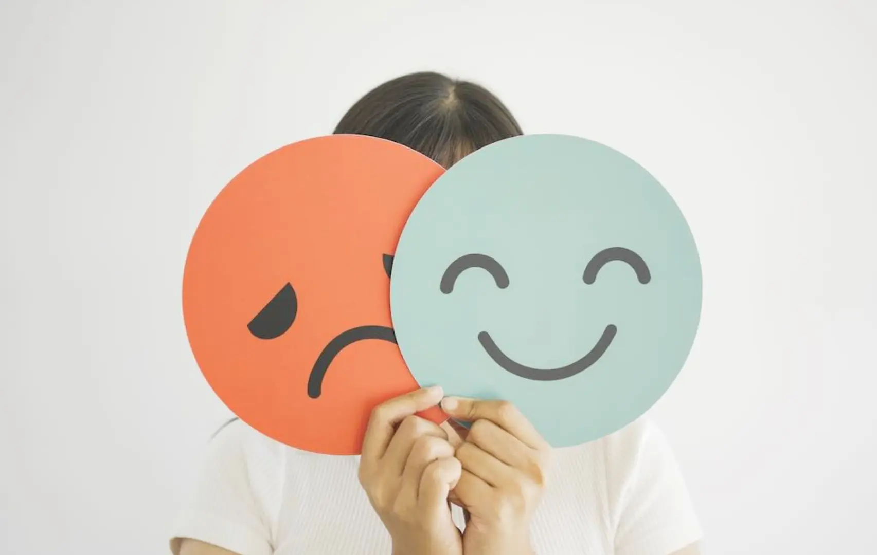 A girl holding up two cards representing a happy and a sad face.