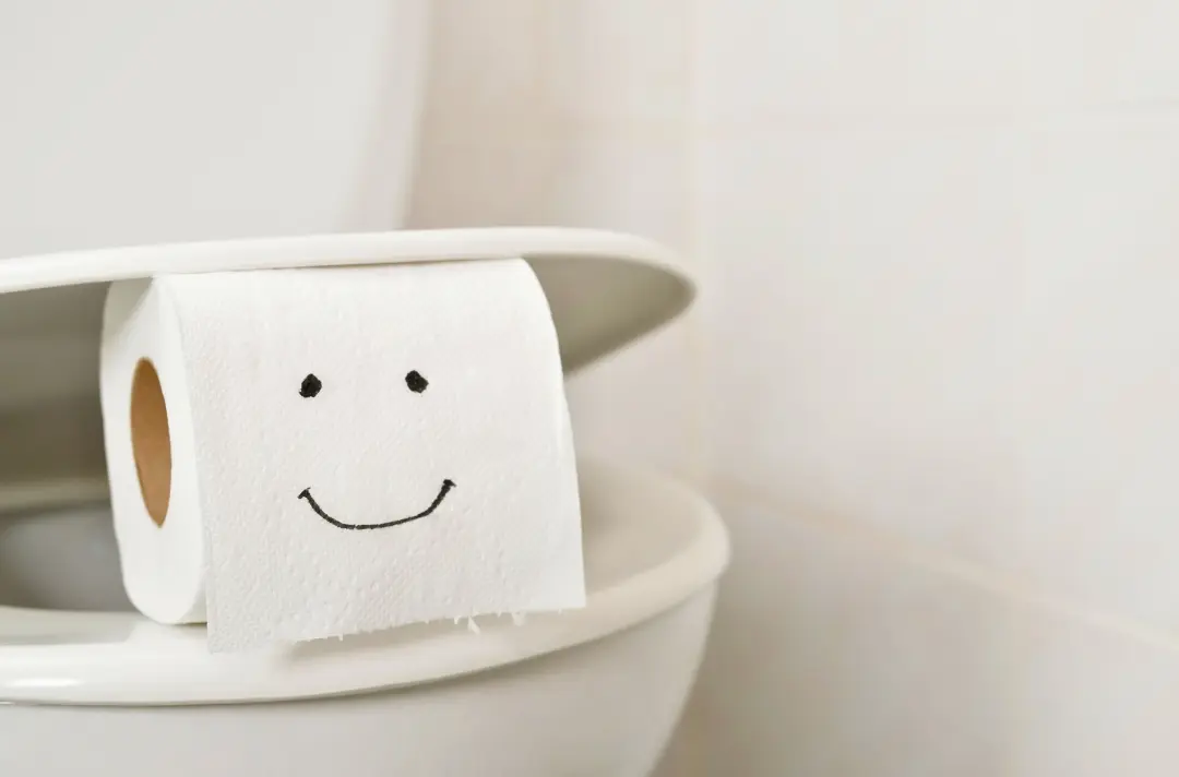 A photo shows a toilet roll sitting on the rim of a sparkling clean toilet. A face has been drawn on the roll.