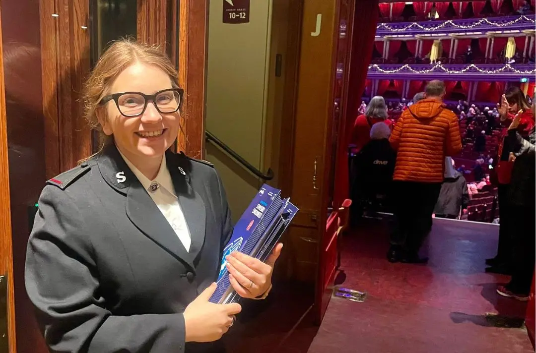 Cadet Beth in Salvation Army uniform standing by the door to the Royal Albert Hall auditorium with programmes for Celebrating Christmas with The Salvation Army