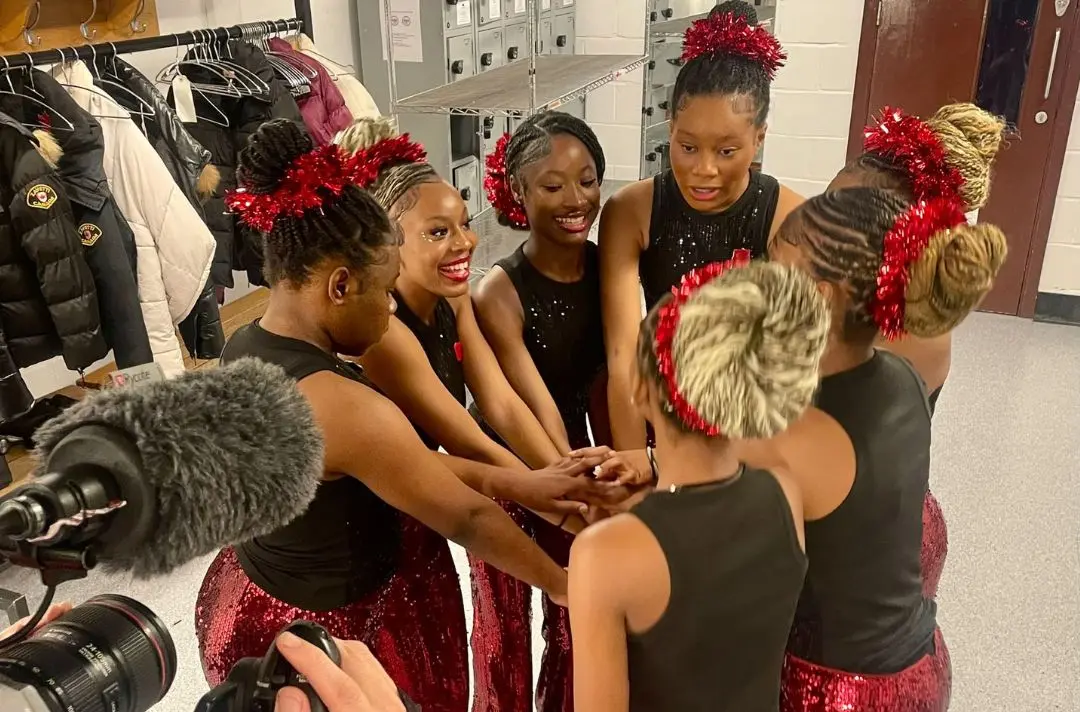 Clapton Dance Group in red sequin outfits backstage share a team high five
