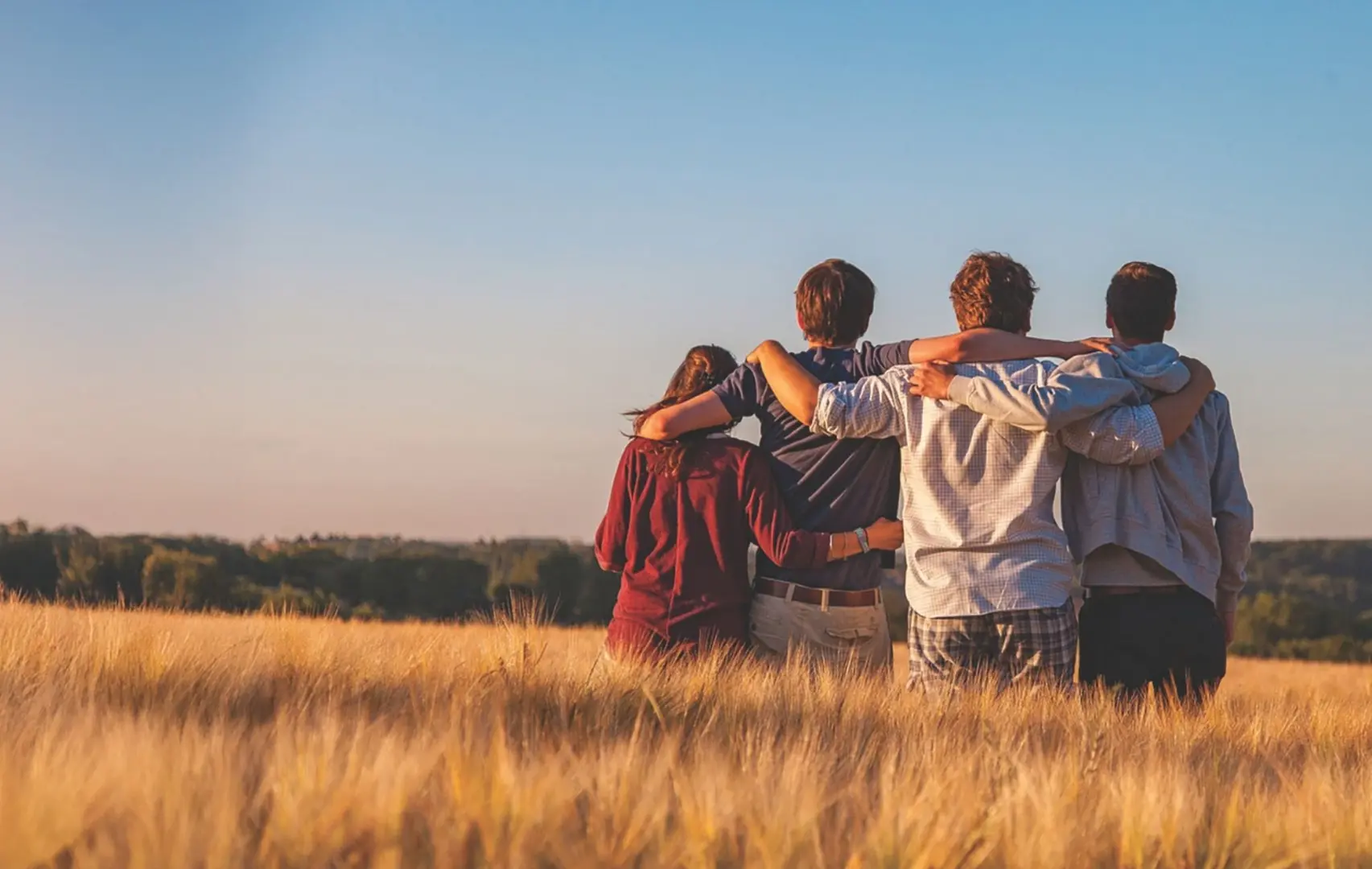 A family with their arms around each others' shoulders in a wheat field.