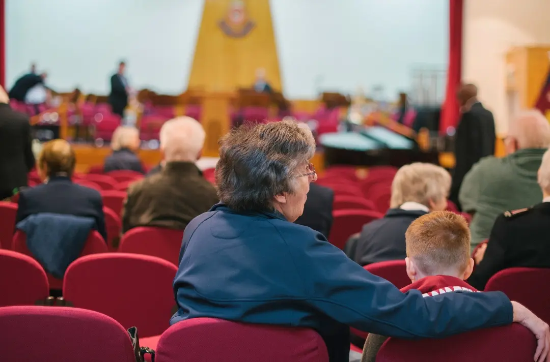 A photo shows two people from different generations sitting side-by-side in a Salvation Army meeting.