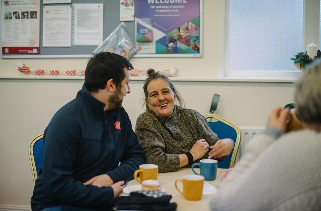 Photo shows two people smiling and laughing while sat at a table.