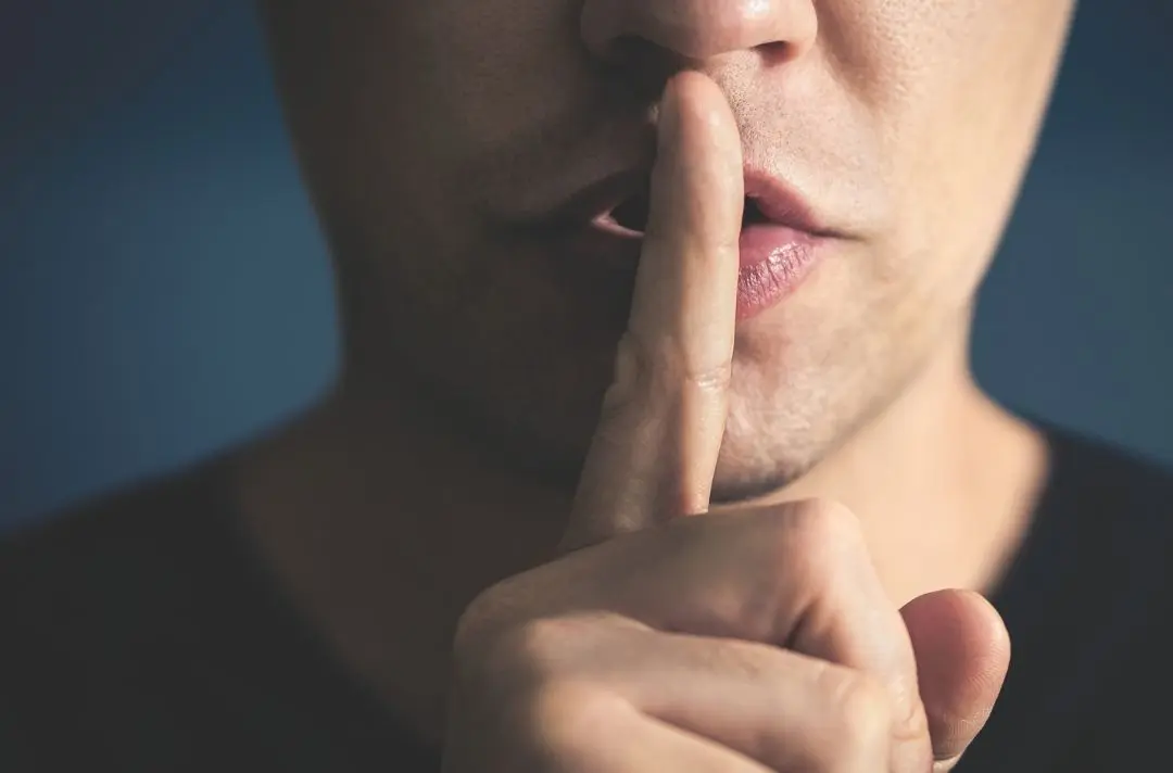 A man putting a finger up to his mouth to indicate silence.