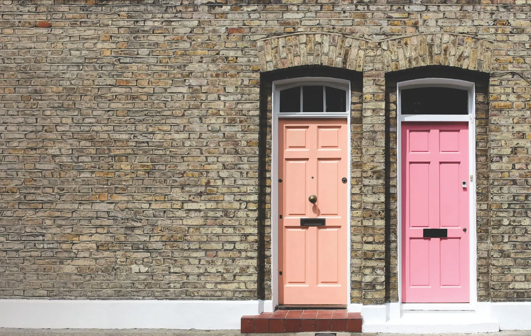 Two pink front doors next to each other against a brick wall backdrop.