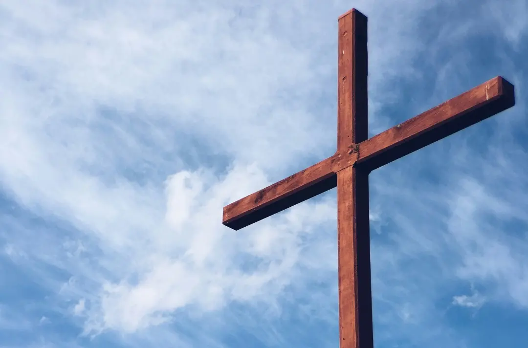 A picture of a wooden cross with a blue sky behind it
