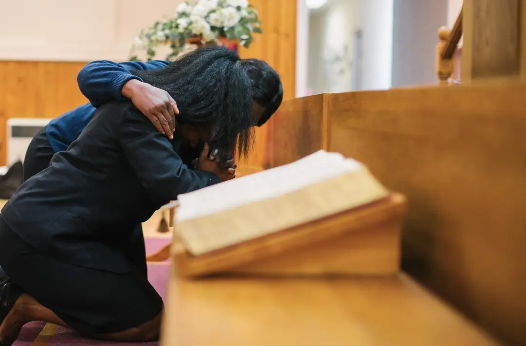 A photo shows two people praying at a mercy seat.