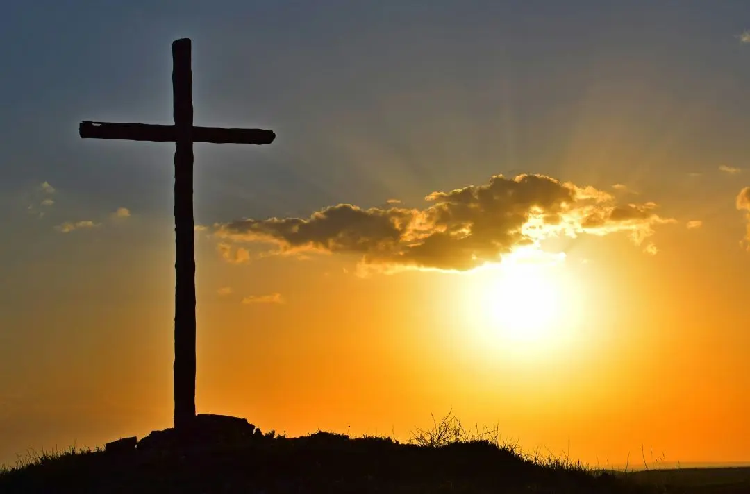 The sun rises behind a cross.
