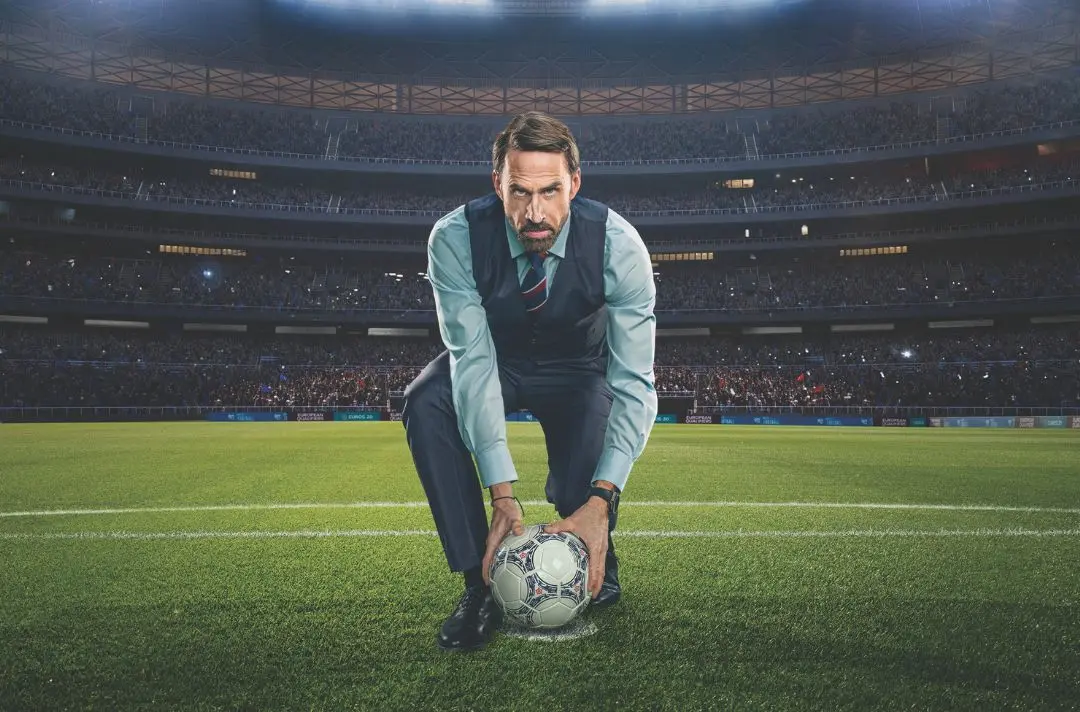 Joseph Fiennes as England Manager Gareth Southgate placing a football onto a grass pitch in a big sports stadium.