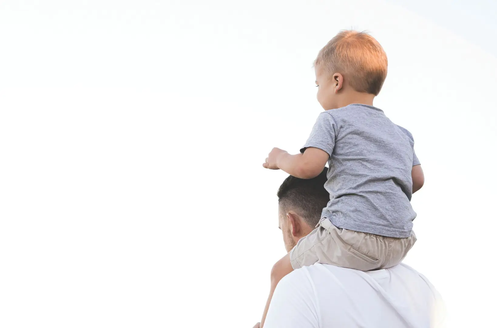 A father carries his son aloft upon his shoulders.