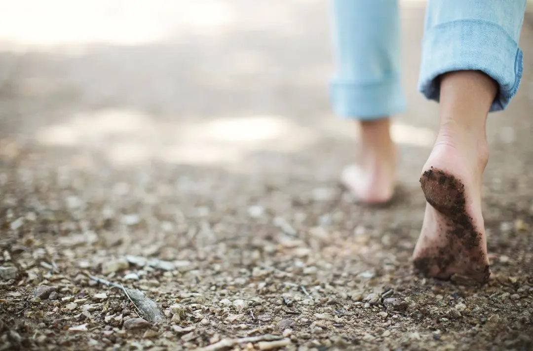 A pair of bare feet walking across sandy gravel.