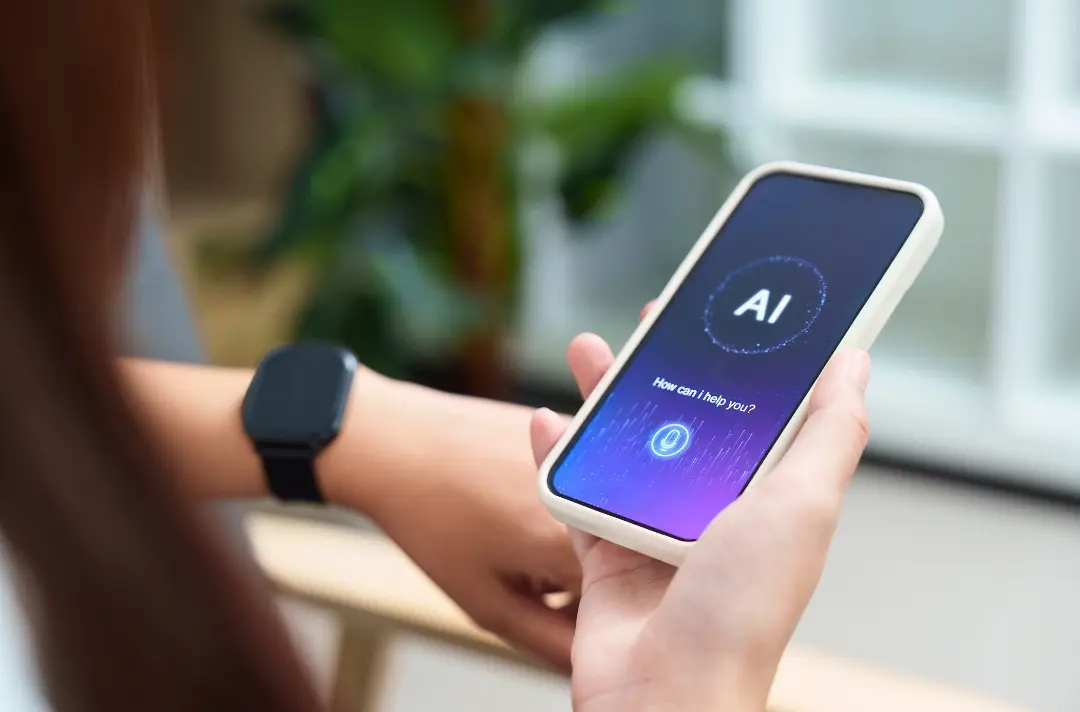 A photo shows someone looking at a phone displaying the text: AI. How can I help you?