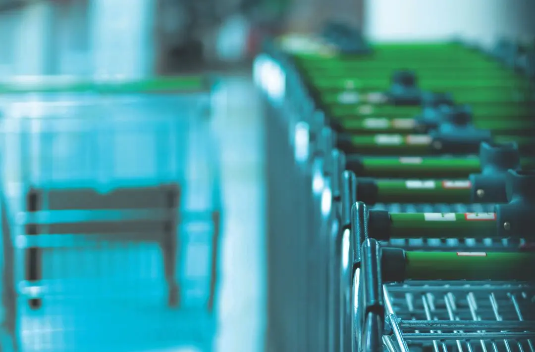 A line of shopping trolleys with green handles.
