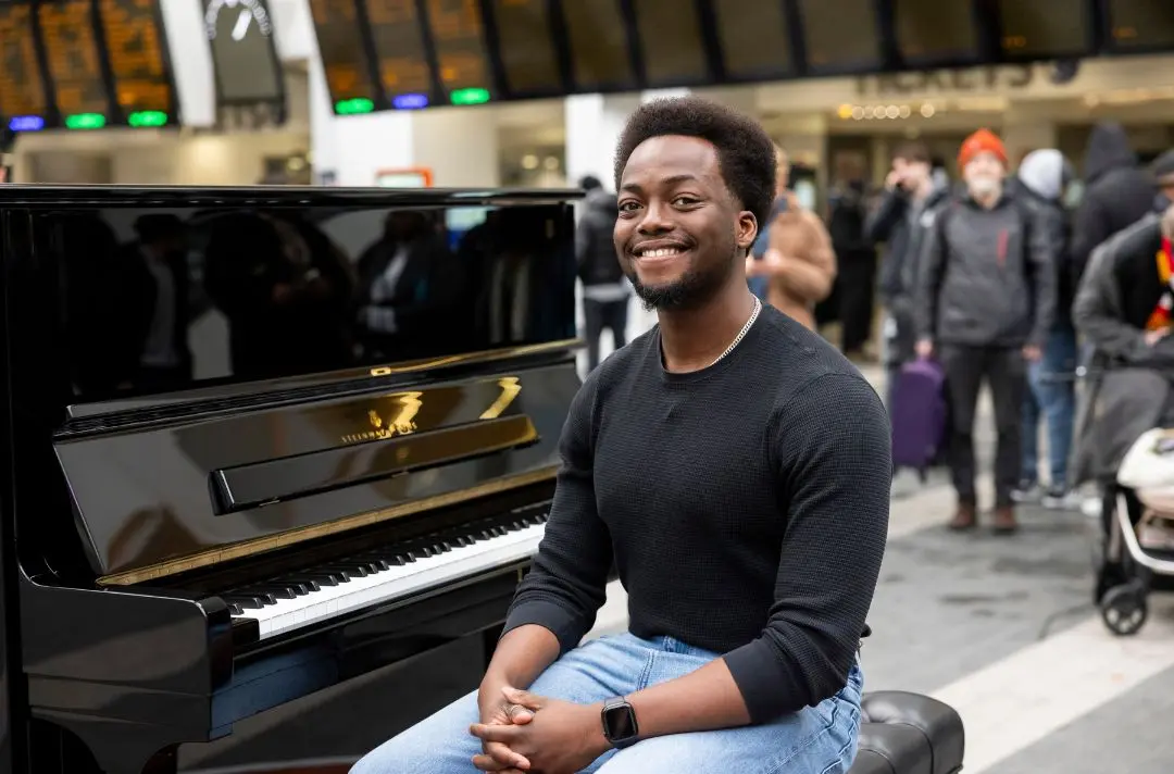 A young male contestant of the new series sits by a piano smiling.