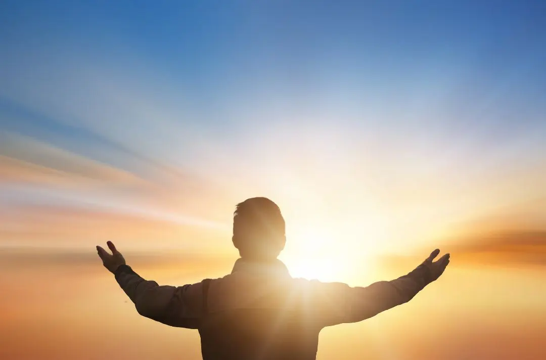 A man holds his hands up to the sky as the sun shines on him.