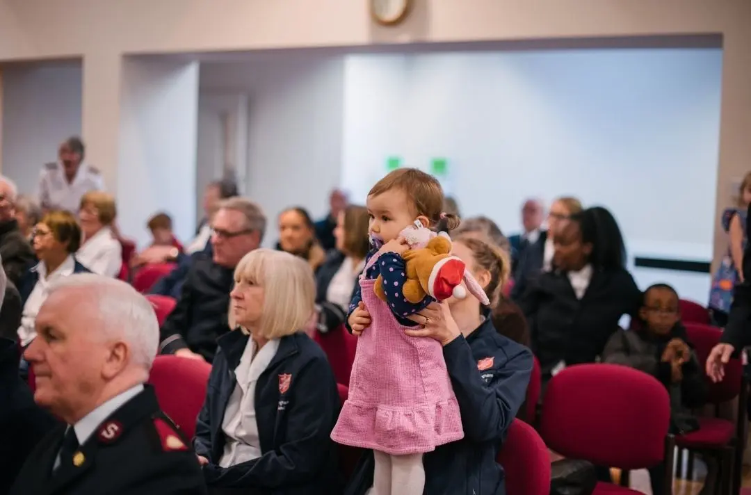 A picture of a child being held up in church surrounded by different generations